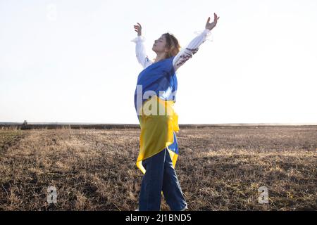 La jeune femme est enveloppée dans un drapeau ukrainien jaune et bleu. Demande d'aide à l'Ukraine, attirant l'attention sur la question du soutien aux Ukrainiens. Indépendants Banque D'Images