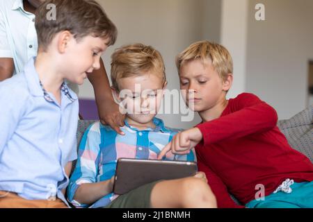 Élèves multiraciaux de l'élémentaire utilisant une tablette numérique tout en étant assis sur un canapé à l'école Banque D'Images