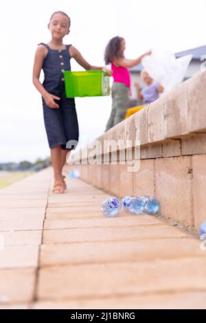 Des écolières élémentaires multiraciales collectent du plastique sur des marches contre le ciel Banque D'Images