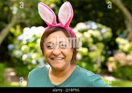 Portrait d'une femme senior afro-américaine souriante portant des oreilles de lapin roses dans l'arrière-cour Banque D'Images