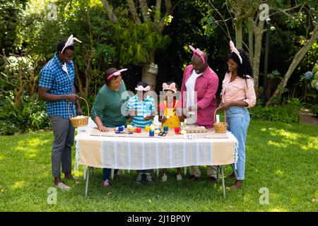 Bonne famille afro-américaine multigénérationnelle dans les oreilles de lapin peignant les oeufs de pâques dans la cour Banque D'Images