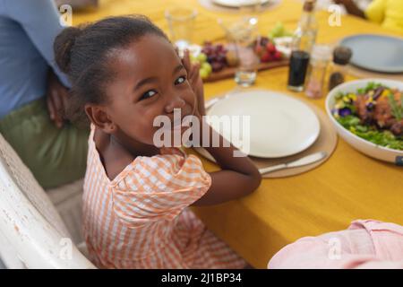 Fille souriante afro-américaine prenant le déjeuner avec la famille à table le jour de l'action de grâce Banque D'Images