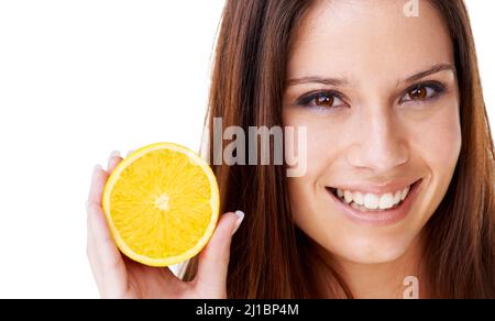 Sa dose quotidienne de vitamine C. Portrait d'une belle femme brune tenant la moitié d'une orange. Banque D'Images