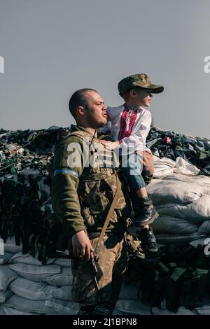 Le guerrier ukrainien de la défense territoriale tient l'enfant garçon dans une chemise brodée dans ses mains sur le point de contrôle. Concept d'invasion militaire russe en Ukraine Banque D'Images