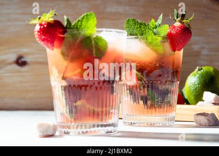 Boisson rafraîchissante d'été cocktail de caipirinha avec fraises et menthe fraîche dans des verres, lumière dure avec ombres Banque D'Images