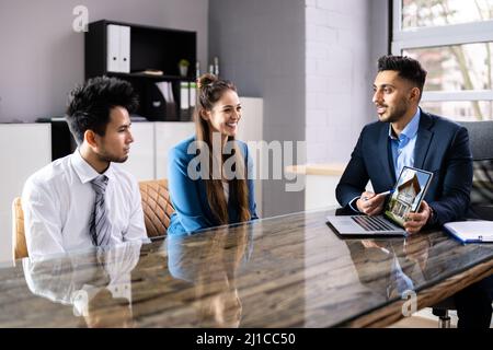 Architect montrant House Model On Laptop To Couple In Office Banque D'Images