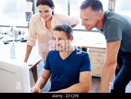 C'est plus facile qu'il ne le pensait au début. Prise de vue de trois collègues regardant un écran d'ordinateur dans un bureau. Banque D'Images