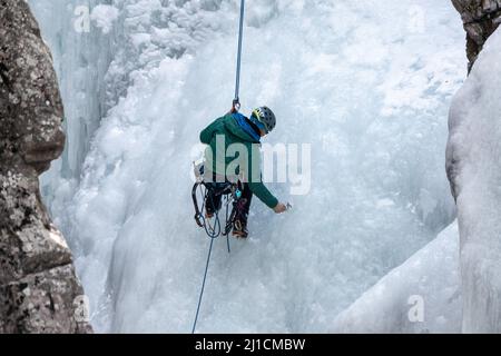 Un grimpeur à glace se visse dans un ancrage à vis de glace alors qu'il descend un mur de glace de 160 pi de haut dans le parc de glace d'Ouray, Colorado, Banque D'Images