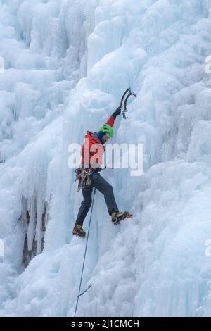 Un grimpeur à glace se visse dans un ancrage à vis de glace alors qu'il mène monte un mur de glace de 160 pi de haut dans le parc de glace d'Ouray, Colorado. Un grimpeur principal n'a pas de t Banque D'Images