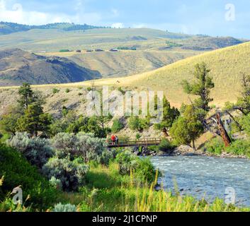 L'homme et la femme se penchent sur une passerelle qui traverse la rivière Gardner dans le parc national de Yellowstone. Le pont est en bois. Banque D'Images