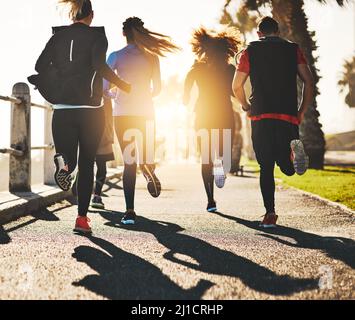 Avoir quelqu'un pour vous motiver fait toute la différence. Vue arrière d'un groupe de remise en forme qui court sur la promenade. Banque D'Images