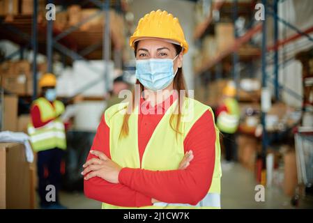 Portrait d'une femme heureuse regardant l'appareil photo dans l'entrepôt Lorsque vous portez un masque facial - concentrez-vous sur le visage Banque D'Images