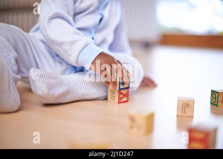 Jouets qui enseignent. Plan court d'un bébé garçon jouant avec des blocs de construction en bois sur le sol. Banque D'Images