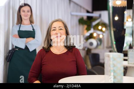 Cliente âgée satisfaite assise dans une chaise de coiffure après coupe de cheveux Banque D'Images