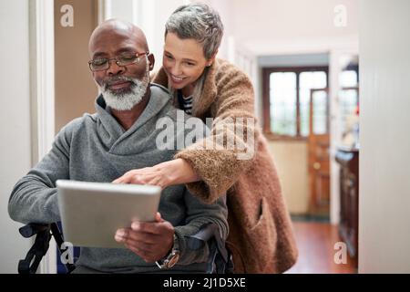 Tout ce qui compte, c'est que c'était ensemble. Prise de vue courte d'un couple affectueux utilisant une tablette à la maison avec l'homme assis dans un fauteuil roulant. Banque D'Images
