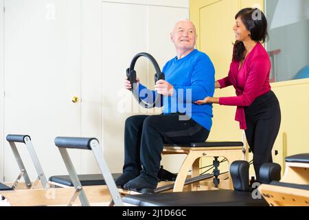 Femme hispanique entraîneur de forme physique contrôle homme âgé s'exerçant avec Magic Circle Banque D'Images