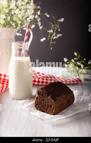 Gâteau au chocolat maison avec glaçage au chocolat et verre de lait sur une surface en bois rustique blanc Banque D'Images