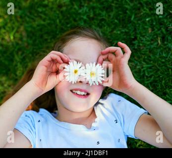 La beauté florissante de la nature. Coupe courte d'une petite fille couvrant ses yeux avec des fleurs tout en jouant à l'extérieur. Banque D'Images