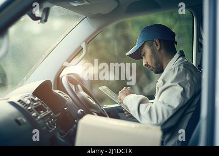 Planifier ses livraisons pour la journée. Prise de vue rognée d'un liveur à l'aide d'une tablette numérique assis dans sa camionnette. Banque D'Images