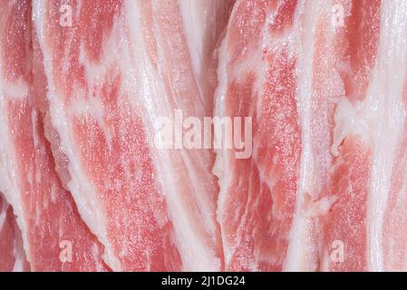 Gros plan vue de dessus pack bacon, morceaux de viande crue de porc rouge frais avec des tranches de graisse blanche sont tranchés en fines bandes empilées l'une sur l'autre Banque D'Images
