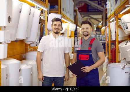 Jeune vendeur et client heureux debout dans l'allée avec chauffe-eau électriques Banque D'Images