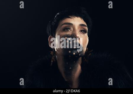 Beauté shinning comme une bougie dans l'obscurité. Photo studio d'une jeune femme posant avec de la peinture sur son visage sur un fond noir. Banque D'Images