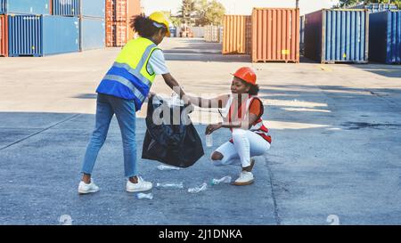 Une femme africaine américaine contremaître ou employée de maintenance a mis sur les casques de sécurité main tenant les ordures sac noir et de partenariat mettant les déchets en plastique wast Banque D'Images