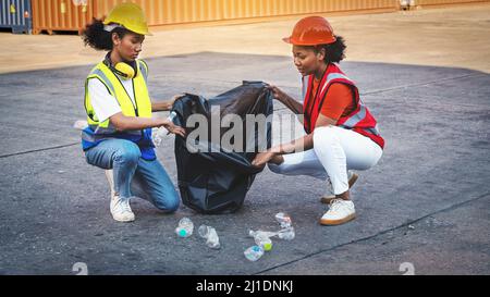 Une femme africaine américaine contremaître ou employée de maintenance a mis sur les casques de sécurité main tenant les ordures sac noir et de partenariat mettant les déchets en plastique wast Banque D'Images