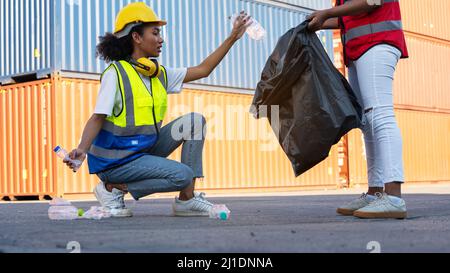 Une femme africaine américaine contremaître ou employée de maintenance a mis sur les casques de sécurité main tenant les ordures sac noir et de partenariat mettant les déchets en plastique wast Banque D'Images