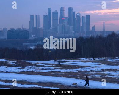 Moscou, Russie. 25th mars 2022. Un homme marche avec son chien à l'aube au parc des collines de Krylatsky sur fond de gratte-ciel de la ville de Moscou. Crédit : SOPA Images Limited/Alamy Live News Banque D'Images