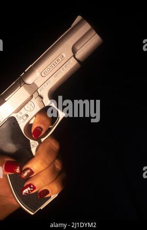 Détective Lady SPY avec vernis à ongles rouge peint tenant pistolet pistolet la nuit Banque D'Images