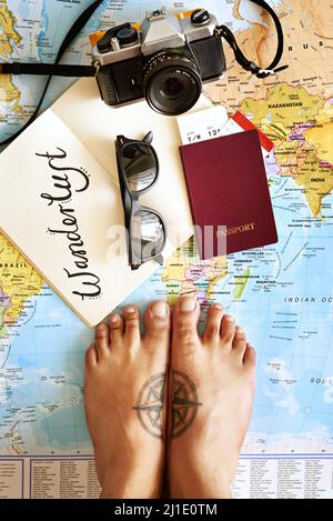 Allez plonger vos pieds dans un océan lointain. Photo en grand angle d'un jeune touriste pieds debout sur une carte avec un carnet, un appareil photo et un passeport disposés dessus. Banque D'Images