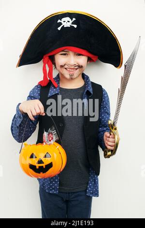 Pirate ludique. Photo d'un petit garçon vêtu d'un costume de pirate tout en tenant une citrouille ou une lanterne sur un fond blanc. Banque D'Images