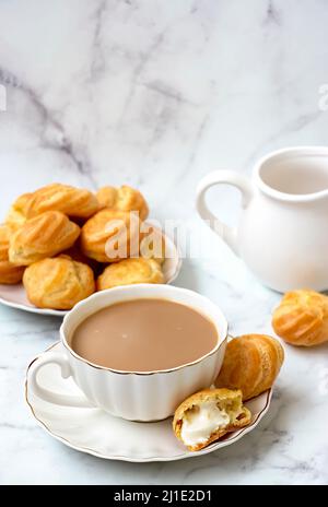 Thé Karak chai ou Masala et profiteroles faits maison farcies de crème fouettée. Sur fond clair de marbre. Banque D'Images