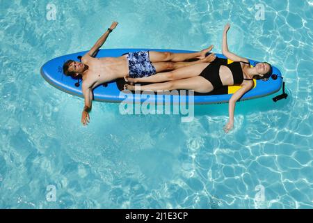 29.07.2021, Italie, Viterbo, Bolsena - jeune couple allongé dans une piscine sur un panneau SUP. 00S210729D196CAROEX.JPG [AUTORISATION DU MODÈLE : NON, PROPRIÉTÉ RELEA Banque D'Images