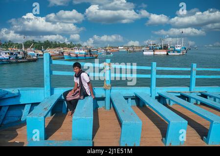Un jeune Indien sur un ferry traversant le Vieux Port de Mangalore (Mangaluru) à Bengre; bateaux de pêche en b/g; Mangalore, Karnataka, Inde Banque D'Images