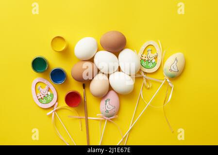 Modèle de thème de Pâques avec œufs de poulet et peintures sur fond jaune. Banque D'Images