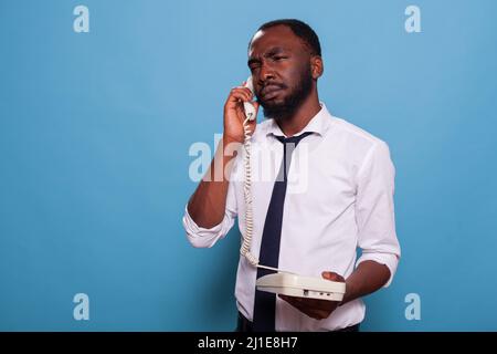 Travailleur de bureau calme tenant le téléphone à cordon en main se concentrant pour écouter la personne à l'autre extrémité de la ligne. Homme d'affaires fatigué à l'écoute de son destinataire au centre d'appels l'ayant mis en attente. Banque D'Images