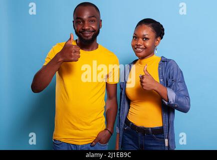 Amateurs optimistes montrant le pouce vers le haut geste pour s'entendre, debout sur fond bleu. Positif homme et femme faisant le bon signe avec les mains, se sentant confiant sur le choix réussi. Banque D'Images