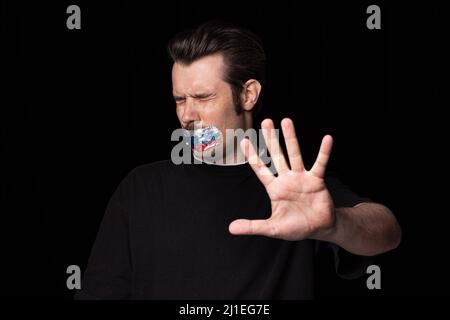 Portrait conceptuel d'un jeune homme avec ruban adhésif de trois couleurs sur sa bouche, isolé sur fond sombre. Censure, concept de liberté de parole. Banque D'Images
