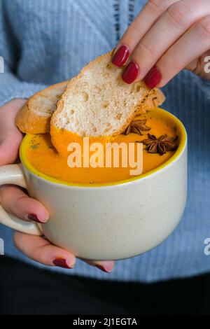 Femme tenant une soupe épicée à la carotte et au gingembre maison. Soupe traditionnelle de citrouille de saison à la texture soyeuse crémeuse. Saine alimentation végétalienne propre. Banque D'Images