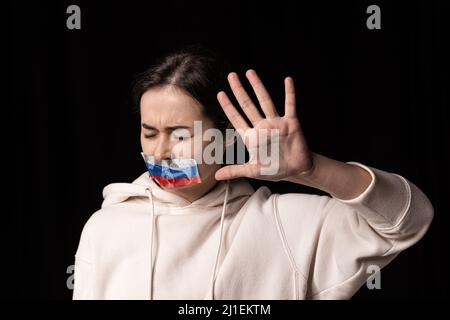 Portrait à demi-jambe d'une jeune fille bouleversée émotive avec ruban adhésif trois couleurs sur sa bouche isolé sur fond sombre. Censure, liberté Banque D'Images