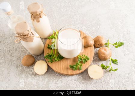 vue de dessus d'un verre rempli de lait de pomme de terre, d'une bouteille de lait de plante et de tubercules de pomme de terre. fond en béton gris Banque D'Images