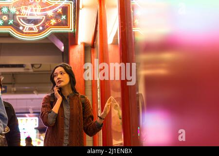 Jeune touriste chinoise parlant sur téléphone portable devant une fenêtre de magasin au marché de nuit - photo de stock Banque D'Images