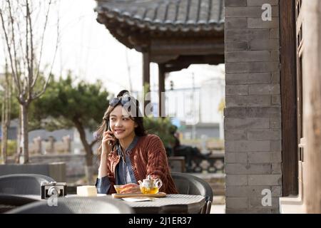 Étudiant chinois appelant un ami et appréciant le thé de l'après-midi dans le café-terrasse - photo de stock Banque D'Images