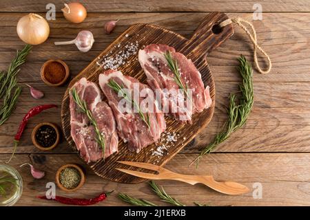 trois steaks de porc de ferme sur une table de cuisson rustique en bois avec des ingrédients. vue sur le dessus. table rustique Banque D'Images