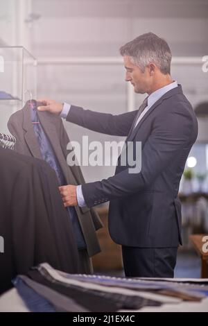 Tu as du s'habiller pour réussir. Photo d'un homme d'affaires mature qui cherche un costume dans un magasin de vêtements. Banque D'Images