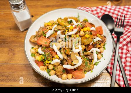 Une délicieuse salade de pommes de terre, de pois chiches, de tomates et de champignons avec persil et aïoli dans un bol avec fourchette et cuillère sur une table en bois. Sain, maison, veg Banque D'Images