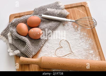 Planche en bois avec œufs de poulet, farine, coeur tiré et fouetter sur fond clair Banque D'Images