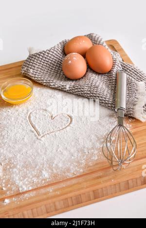 Planche en bois avec œufs de poulet, farine, coeur tiré et fouetter sur fond clair Banque D'Images